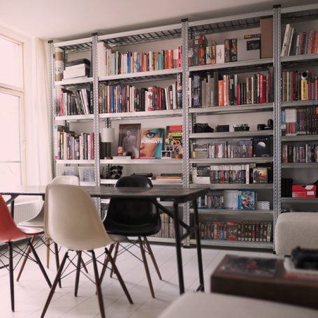 Stijlvol voor jouw woonkamer. Moderne woonkamer met een tafel, stoelen en een stellingkast als boekenkast vol boeken en spellen.